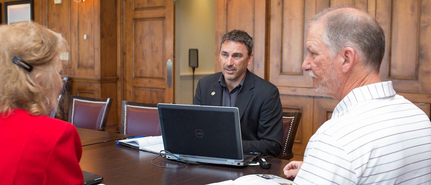 three adults seated at a table, one with an open laptop in front of him